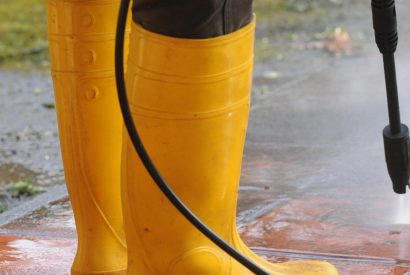 A person wearing yellow rubber boots with high-pressure water nozzle cleaning the dirt in the tiles